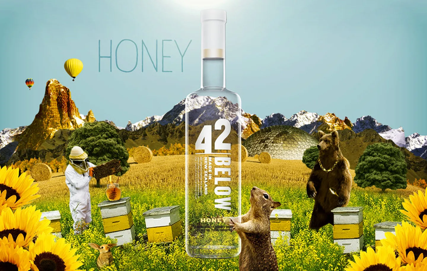 42Below Honey flavour world — bottle in a golden field of sunflowers and beehives, with a beekeeper, a bear wearing a gold chain, a squirrel, and hot air balloons against mountain backdrop