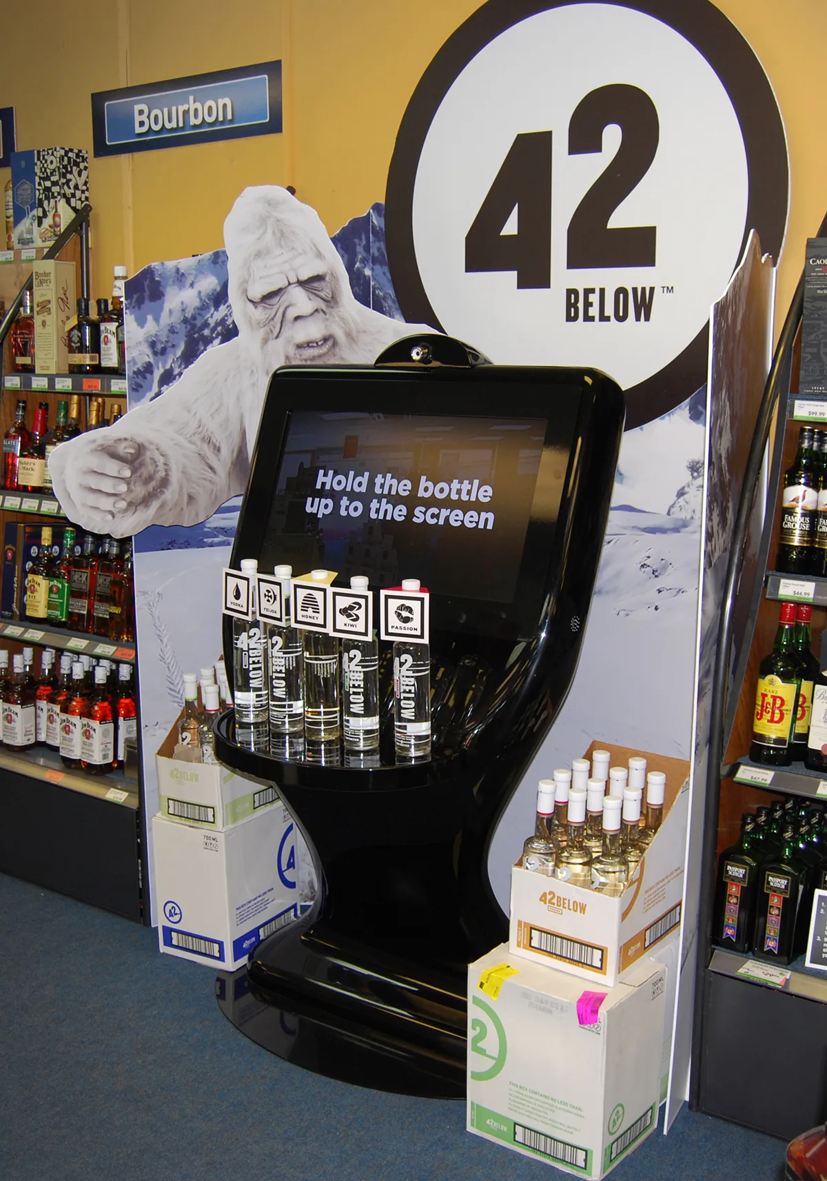 The 42Below Fat Boy AR kiosk in a Liquorland store, showing the webcam screen with 'Hold the bottle up to the screen' prompt, surrounded by 42Below bottles